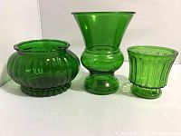 Photo showing three green glass vases with varying shapes and ribbed patterns.