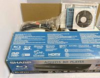 Original box of Sharp Aquos BD-HP25U Blu-Ray disc/DVD player featuring logos and specifications, with included manuals and software CD shown on top.