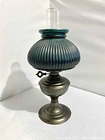 Photo of hunter green ribbed glass shade oil lamp with metal base on white background showing lamp from front angle.