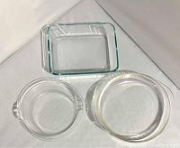 Top view of three Pyrex baking dishes: rectangular, round, and pie plate; all clear glass with some scratches and signs of use.