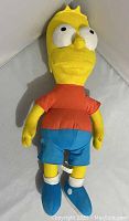 Full view of Bart Simpson cloth stuffed doll wearing red shirt, blue shorts, and blue shoes, showing wear consistent with age and use.