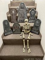 Seven-piece Halloween set displayed on carpeted stairs including six styrofoam tombstones and one seated plastic skeleton with detached hands.