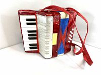 Front side of the red vintage children's accordion showing piano keyboard and strap.