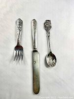Photo of the small Peter Rabbit fork, the Puss in Boots spreader, and the 1976 Christmas collectible spoon showing their size and design details.