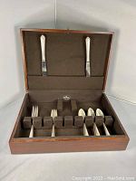 Wooden box open showing set of silver-colored flatware in fabric-lined slots including forks, knives, and spoons.