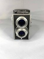 Front view of the vintage Super Ricohflex twin-lens reflex camera. Shows two lenses vertically aligned, textured black body, and Ricoh branding on front plate.