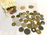 Wide view of the collection including brass tokens, medallions, and coins spread around a cloth bag.