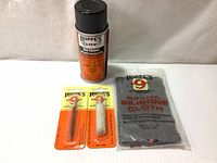 All four main cleaning items displayed together: Hoppe's 9 Elite Cleaner aerosol can, phosphor bronze brush and cotton swab in packaging, and silicone cloth pack.