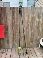 Full height view of Primos Trigger Stick Gen 2 bipod standing fully extended against wooden fence with accessory packaging on the ground.