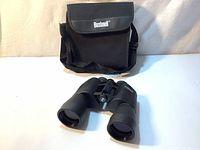 Front view of Bushnell binoculars in front of the black carrying case showing the overall condition and appearance of both items.
