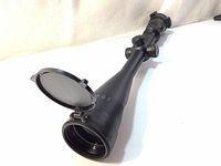 Bushnell ENGAGE riflescope showing the objective lens with flip-up lens cover open and visible dents on the scope tube.