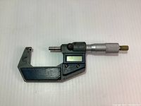 Photo showing one full micrometer with digital display and adjustment mechanism, featuring a metal body and a brass end cap.