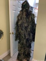 Full view of the ghillie suit worn on a mannequin showing jacket with hood, pants, and overall leafy camouflage knit material.