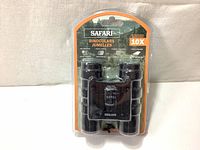 Front view of Safari binoculars in sealed orange and black blister packaging showing overall condition and branding.