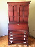 Closed view of tall ruby finished hutch secretary with double doors, slant front desk, and four lower drawers with large handles.