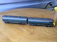Two Canadian National model train pieces side by side on a wooden surface, showing the full length of both engine and car with detailed roof and side paintwork.