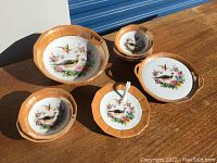 Photo of five German porcelain dishes with bird and floral designs on a wooden table, items show signs of wear and use.
