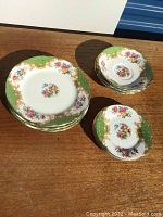 Set of plates with floral design, gold scrollwork, and green border laid on wooden surface