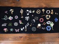 Overview of over 30 assorted brooches, pins, and earrings on black cloth