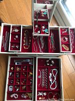 Image of multiple open compartments in a red velvet jewelry box showing wrists watches, chains, brooches, earrings and pins.