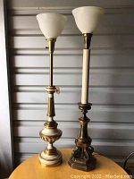 Both lamps shown together on round wooden table inside storage unit, highlighting size difference and overall condition.