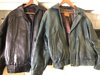 Two leather jackets, one black with zipper and textured elastic cuffs/waistband, one green with snap button and stitching details