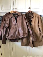 Three leather jackets hanging on wooden hangers against a white cabinet background, showing front view with their collars and sleeves visible.