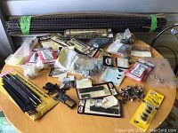 Full lot of various model train parts and track pieces spread on a wooden table, including packaged and loose items.