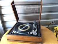 Photo showing the open record player with dust cover open, tonearm and platter visible.
