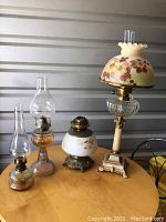 Full view of four oil lamps on table, showing their height and decorative details