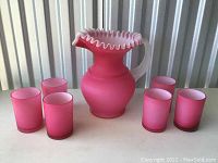 Full set of pink glass pitcher and six matching glasses arranged on table, showing the complete lot