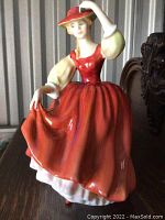 Front view of the Royal Doulton "Buttercup" figurine showing the woman in red dress and cream sleeves lifting her skirt and holding hat.