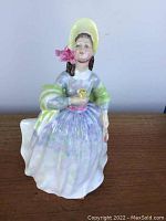 Front view of the Royal Doulton Clare figurine showing detailed face, bonnet with pink ribbon, and colorful dress with green shawl.