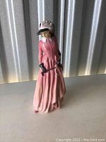 Front view of Royal Doulton porcelain figurine Maureen dressed in pink with black gloves and hat.