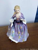 Front view of Royal Doulton Nicola figurine showing detailed porcelain figure in purple floral dress holding a bird.