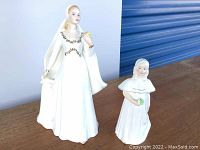 Front view of the Royal Doulton Bride and Bridesmaid figurines side by side on a wooden surface with blue background.