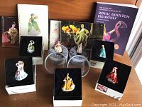 Eight Royal Doulton Miniature Ladies porcelain figurines arranged on a table, each figurine in black display box, surrounded by related booklets and catalogues.