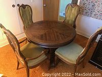 Full view of round hardwood dining table and four matching upholstered chairs around it.
