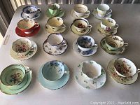 Overview of 16 assorted tea cups and saucers arranged on tabletop