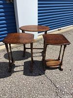 Three wooden accent tables grouped outdoors against storage units