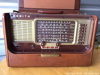 Front view of the Zenith Trans Oceanic radio inside tan leather case, showing dial, buttons, speaker grille, and Zenith branding.