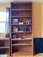 Front view of a tall, wooden bookcase filled with books and photo frames, showcasing the adjustable shelves and overall condition.