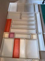 Top-down view of all 23 drawer organizers arranged on the floor showing different sizes and colors mostly white with some orange and pink pieces.