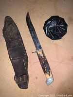 Photo of hunting knife, leather sheath and black leather coin purse on a flat surface