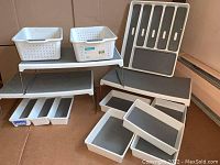 Overview photo showing most items: two white perforated baskets on a white shelf, trays, stands, and drawer organizers arranged inside a box.