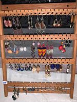Full view of wooden earring rack filled with assorted earrings of varied styles, colors, and materials.