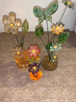 Full view of three Lucite flower arrangements in amber vases on table, showing metal wire stems and colorful translucent petals and leaves