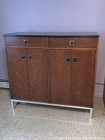 Front view of credenza closed showing black top, bookmatch veneer doors, two drawers and chrome base