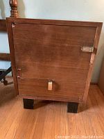 Front view of nightstand with door closed, showing wood veneer, metal pull at center bottom, scratches and wear.