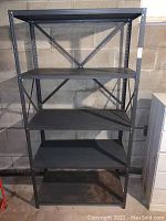 Front view of the full gray metal utility shelving unit showing all four shelves and the sturdy frame against a concrete wall.